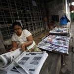 A woman arranges newspapers to sell by the street side in Yangon