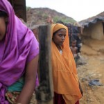 Rohingya women stand in front of their makeshift home in an unregistered Rohingya refugee camp in Teknaf