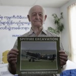 Stanley Coombe poses with a picture of a Spitfire fighter plane after a news conference at the Parkroyal hotel in Yangon