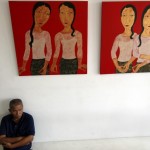 Artist sits under paintings in an art gallery in Yangon