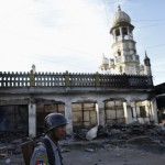 A police officer stands near a mosque which was burnt during a riot between Buddhist and Muslims in Lashio township