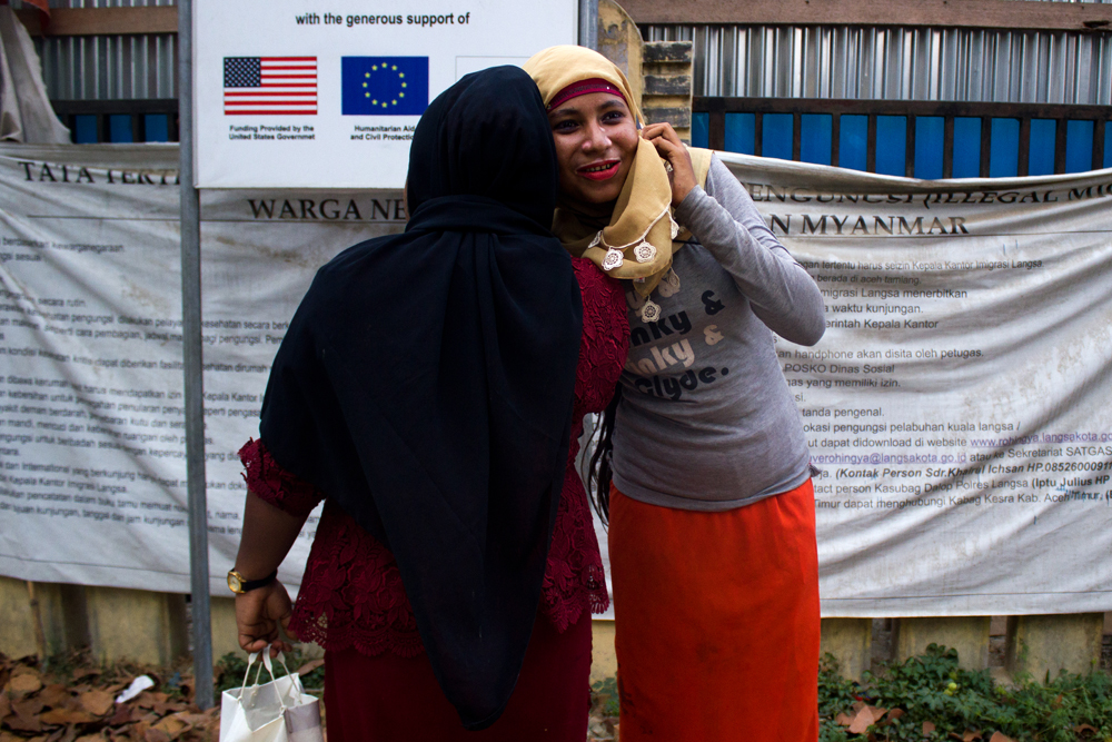 Two Rohingya women speak on the phone with their relatives in Burma at the entrance of Lhok Bani Refugee Camp, in Langsa City (Aceh Province, Indonesia). Photo: Carlos Sardiña Galache / Yayasan Geutanyoe – A Foundation for Aceh.